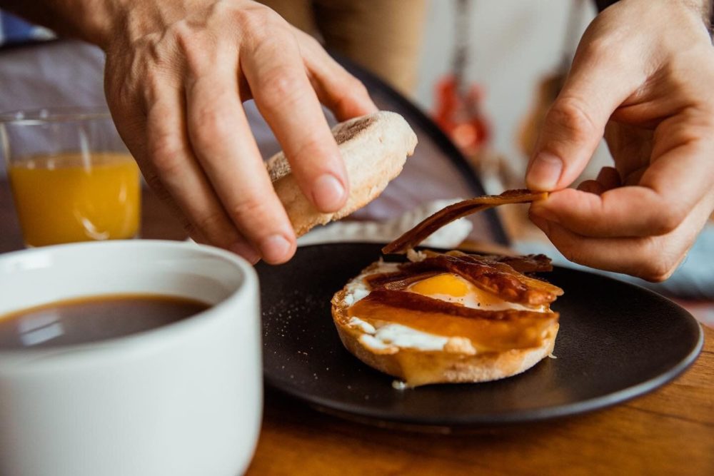 Close-up of someone putting Umaro bacon on a breakfast sandwich